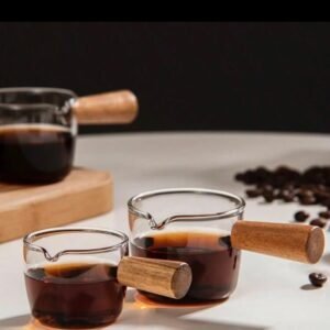 High borosilicate glass jug with a small wooden handle, for whipping milk, serving espresso and a small sauce plate, and a milk jug used in restaurants