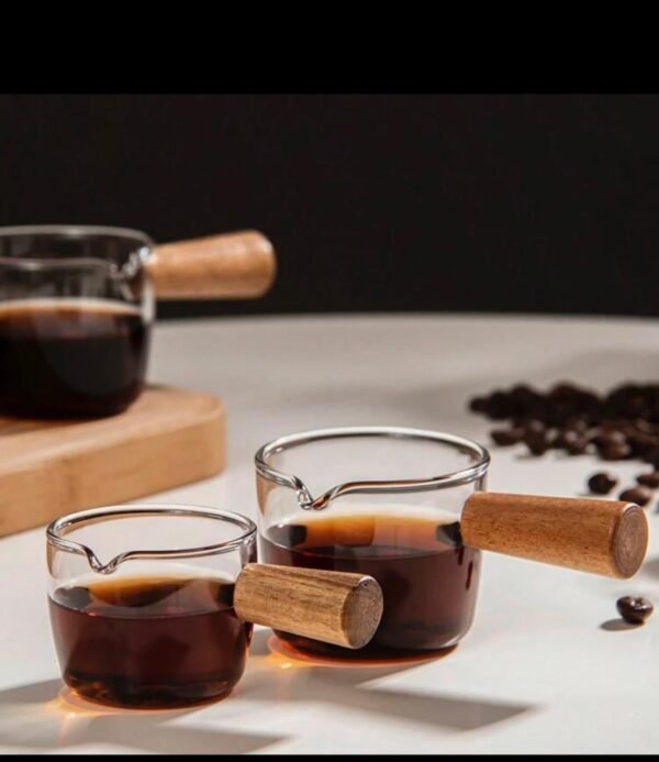 High borosilicate glass jug with a small wooden handle, for whipping milk, serving espresso and a small sauce plate, and a milk jug used in restaurants